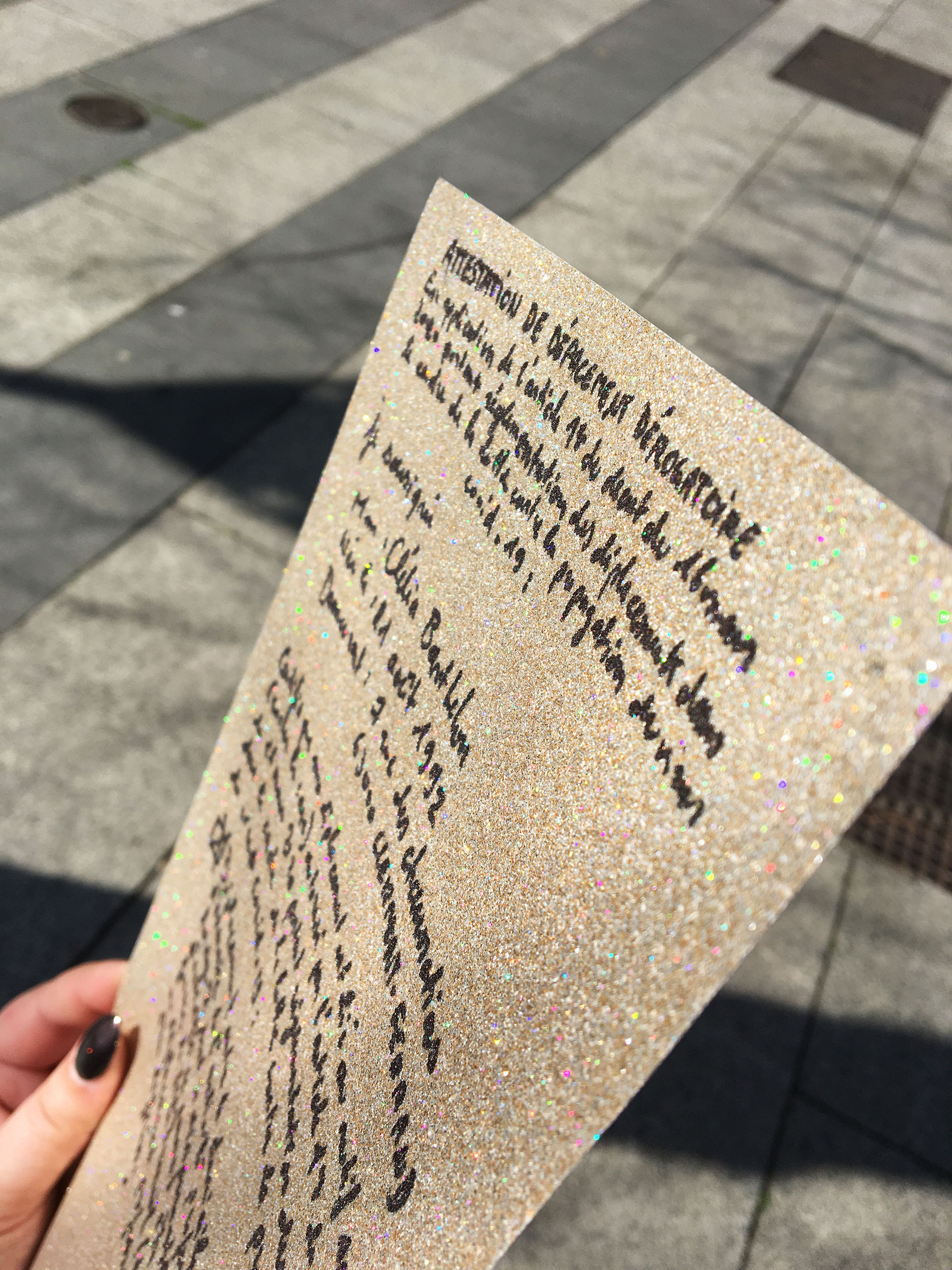 Photo prise à l'extérieur, sur une feuille pailletée on voit écrit à la main une attestation de déplacement dans la periode du Covid au nom de Clélia Barthelon.