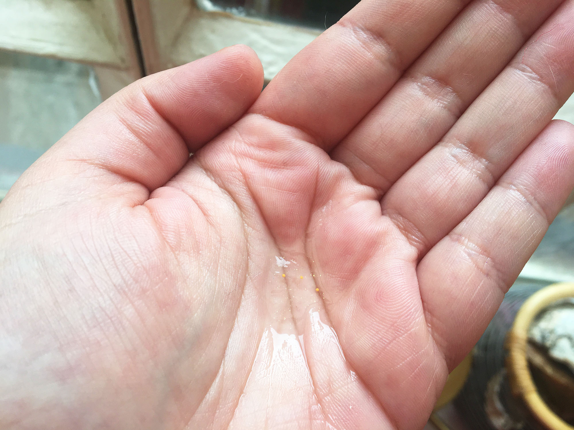 Dans une main ouverte, un petit peu de gel hydroalcoolique a été versé. À l'interieur du gel il y a des paillettes.