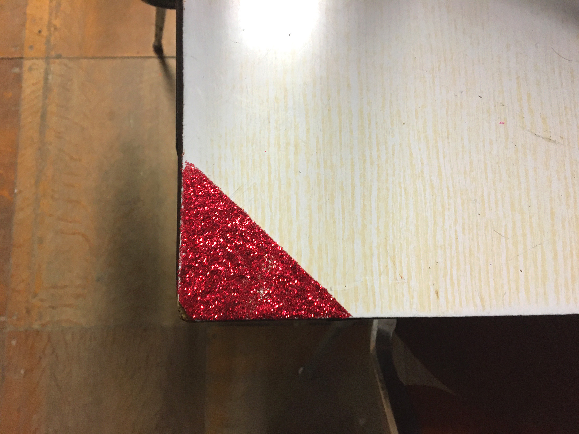 Gros plan sur un des angles de la table, un triangle rouge de paillettes est collé.