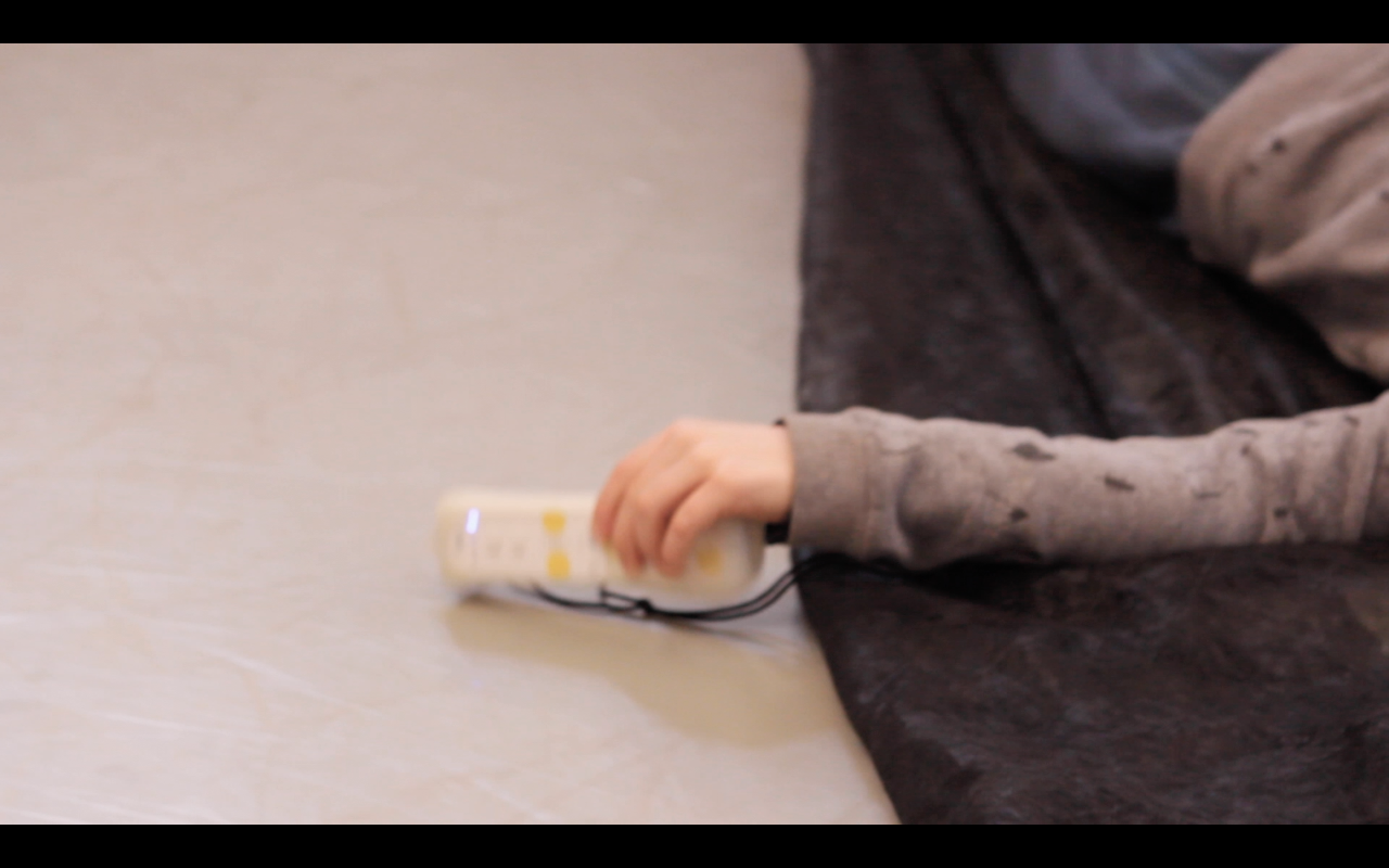 Un enfant est allongé sur un tissu, on e voit que son bras qui tiens une manette de wii qui a une forme de télécommande qu'il frappe au sol.